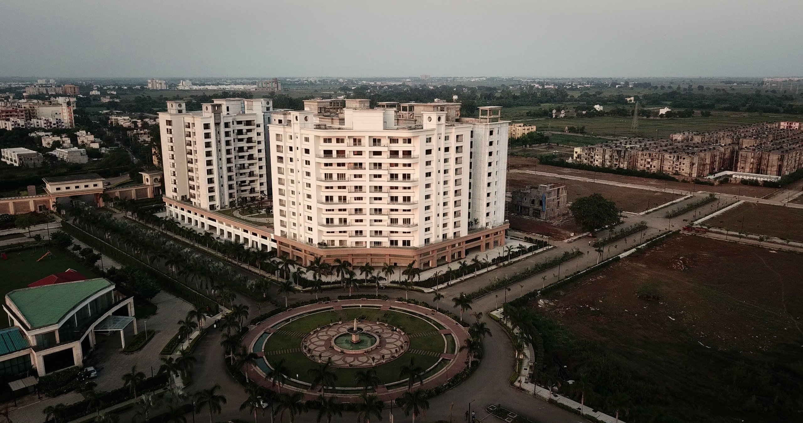Anandam World City at dusk — the central fountain roundabout, clubhouse and residential towers